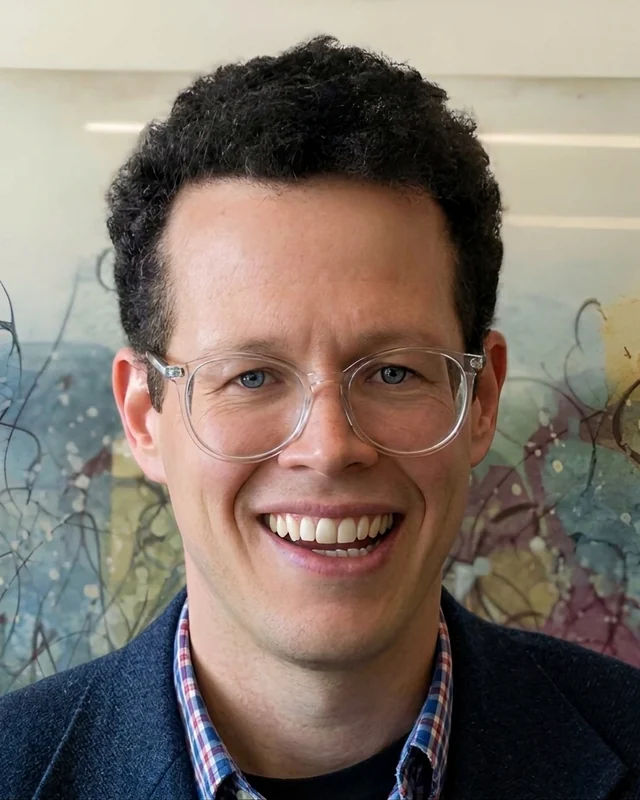 Jamie Hanson, smiling, wearing clear-framed glasses and a navy blazer