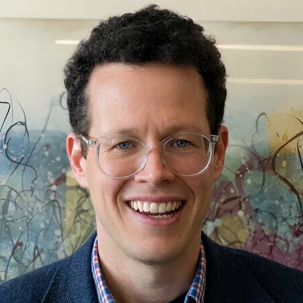 Jamie Hanson, smiling, wearing clear-framed glasses and a navy blazer